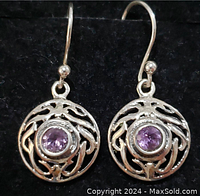 Front view of pair of sterling silver earrings each featuring a swirling openwork design with round bezel-set purple amethyst gemstone in center on hook posts.