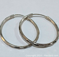 Pair of sterling silver hoop earrings with hammered finish, visible hinged clasp, on a white background.
