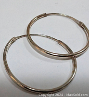Close-up photo of pair of smooth, shiny sterling silver medium-sized hoop earrings laid flat on white background.