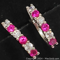 Close-up front view of the sterling silver earrings with alternating ruby and CZ stones against black background.