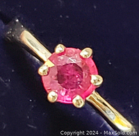 Close-up photo of the ruby ring showing the six gold-toned claw prongs securing the deep red round ruby on a polished sterling silver band.