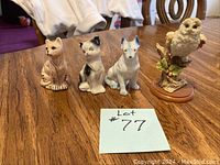 Four animal figurines on wooden table: two cats, one dog, one owl, with lot number card.