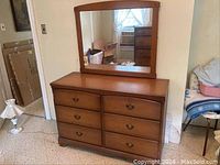 Solid wood bureau with six drawers and attached mirror in a room.
