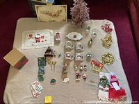 Photo showing a Christmas-themed lot with cups, a small pink metallic tree, figurines, wreaths, towels, and cards arranged on a beige cloth.