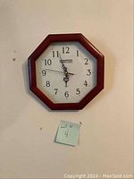 Octagonal wooden frame battery powered wall clock with white face and black numbers hung on a wall, showing wall clock face clearly with visible clock hands pointing near 12:30.
