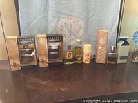 Full lot of 8 cologne and perfume bottles with some in original boxes and others loose on a wooden surface against a blue fabric background.