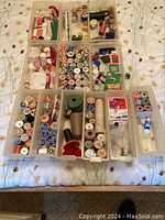 Overview of multiple plastic boxes filled with various sewing supplies including spools of thread, buttons, and sewing notions laid out on a fabric surface.