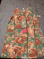 Full view of sleeveless floral dress laid flat on a carpet, showing front and overall pattern and shape.