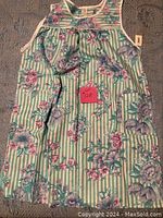Front view of sleeveless striped green and white dress with floral print and a pink tag with lot number.