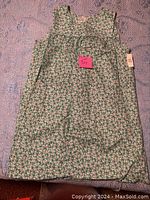 Full view of the green floral sleeveless dress laid flat on a purple textured surface with a pink price tag.