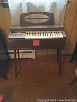 Full view of the vintage electric chord organ standing on four angled wooden legs with an integrated music stand on top.