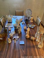Wide view of all items on a wooden table including figurines, plaques, plate, mugs, glass vases and anniversary collectibles