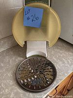 Manual operated white and yellow Kitchen Magic food processor with metal grating and slicing disc in front.