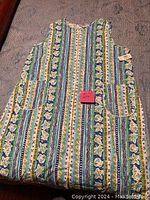 Sleeveless multi-patterned house dress with large front pockets laid flat.