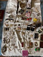 Photo showing a wide variety of costume jewelry including earrings, bracelets, brooches, necklaces, pendants, a watch, and boxed jewelry on a white textured surface.