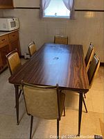 Full view of the kitchen table with six chairs arranged around it in a tiled room near a window.
