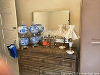 View of lamps on wooden dresser showing three sets of blue floral glass and ceramic lamps and one individual lamp with two pleated fabric shades.