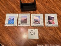 Five square photo sentiment coasters with scenic images and inspirational words arranged on a wooden surface, alongside a note with lot number.