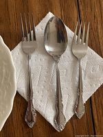 Three utensils including two forks and one spoon with ornate floral design on handles placed on a white paper towel.