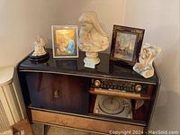 Five religious items including three statues and two framed pictures displayed on a vintage radio console