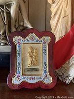 Close-up of framed religious plaque with 'PROTEGGIMI' inscription and floral border