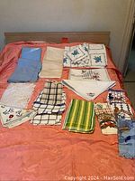 Photo showing full assortment of table cloths, napkins, and dish towels neatly arranged on orange table cloth covering bed.