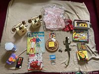 Overview photo showing all items in the lot arranged on a blanket including toy phones, pattern book, fan, lizard toy and other small items.