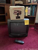 Front view of Daewoo CRT TV with remote control on carpet and deluxe indoor color TV antenna box on top of the TV.
