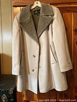Beige winter coat hanging on wall, showing front with soft faux fur collar and button closure.