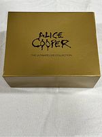 Gold box with Alice Cooper The Ultimate Live Collection text on the top, closed.