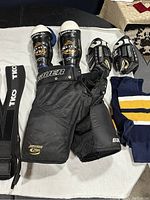 8 pieces of hockey equipment laid out including pants, gloves, shin guards, socks, and belt showing brand logos and size labels.