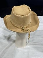 Front angled view of tan suede cowboy hat showing braided band and metallic accent