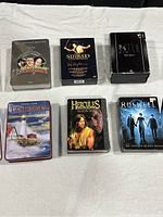 Six DVD box sets laid out on a white cloth featuring The Three Stooges, Sinbad, The X Files, Lighthouses of America, Hercules Season One, and Roswell Season Two.