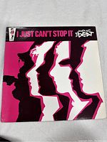Front cover of the vinyl record 'I Just Can't Stop It' by The English Beat showing stylized pink and black graphic art of band silhouettes.