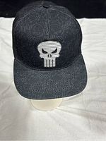 Front view of black Marvel Punisher cap showing large white Punisher skull logo embroidered on front panel and tonal all-over pattern of smaller skull logos.
