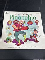 Front cover of the vinyl record showing colorful illustrated characters Geppetto and Pinocchio with cuckoo clocks and goldfish bowl, title text 'Walt Disney's Pinocchio' and song titles.