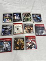 Photo showing 11 PS3 game cases arranged on a white cloth, covers visible for identification.