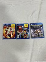 Three PS4 game cases laid flat, showing LEGO The Incredibles, LEGO Movie Videogame, Destiny 2 covers with sale stickers on two cases.