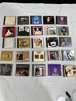 Full view of 26 vintage CD cases arranged in rows on a white surface showing album artwork and labels.