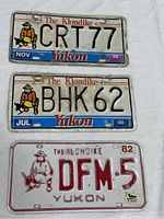 Front view of three Yukon license plates dated 1982, 1999, and 2000 with 'The Klondike' text and stylized man with pickaxe logo.