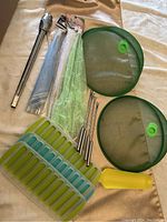 Full view of all BBQ and food covers, tongs, skewers, and ice trays in lot on beige fabric surface