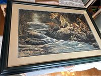 Front view of large framed wall art showing cheetahs by river with dark green frame and matting.