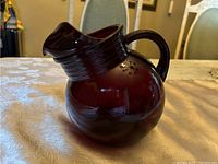 Photo showing the front and side view of the dark red cranberry glass pitcher with round body and curved handle.