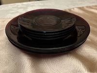 Stack of cranberry glass plates showing 3 larger plates on bottom and 4 smaller plates on top, all with deep reddish-purple color and glossy finish.