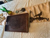 Photo showing all lot items including green-yellow glass vase, wood tray with carved pattern and chip, wind chimes with wooden top, and wrought iron bird plant holder.