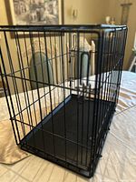 Full view of the black metal wire dog cage placed on a table, showing cage structure and door latch.
