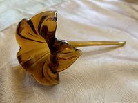 Side view of amber-coloured glass flower showing the curved stem and ruffled petal edges.
