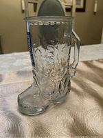 Clear glass cowboy boot mug sitting on a table showing side view with handle.