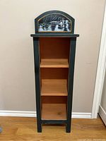 Front view of wooden shelf painted dark green with natural wood shelves and hand painted duck scene on arched top panel.