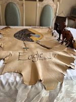 The same leather eagle artwork visible with focus on the entire piece showing feather and bone detail.